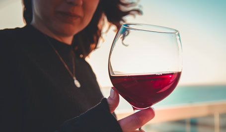 Frau, die am Strand steht und ein Glas Rotwein in der Hand hält