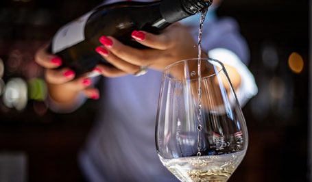 Frau mit roten Fingernägeln, die eine Flasche Wein hält und Weißwein in ein Weinglas einschenkt