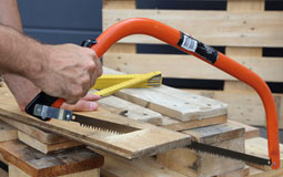 Kleine Grafik zum Thema Werkzeug mit einer orangenen Handsäge, die ein Holzbrett durchsägt