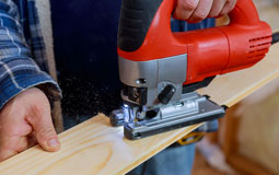 Kleine Grafik zum Thema Werkzeug mit einer roten Stichsäge, die ein Holzbrett durchsägt