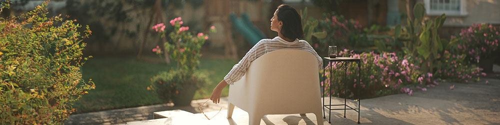 Frau sitzt in einem weißen Gartenstuhl auf der Terrasse 