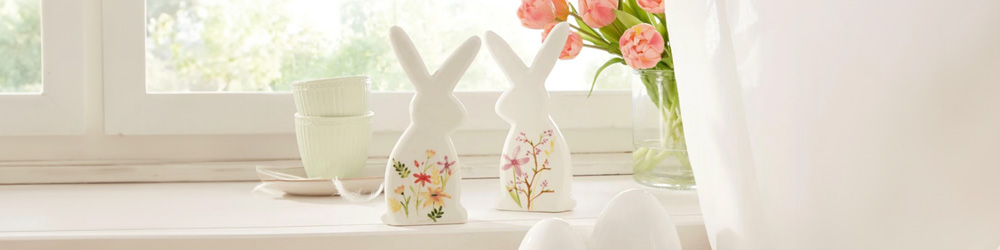 Zwei weiße Osterhasen aus Porzellan mit bunten Blumen bemalt stehen auf einem Fenstersims